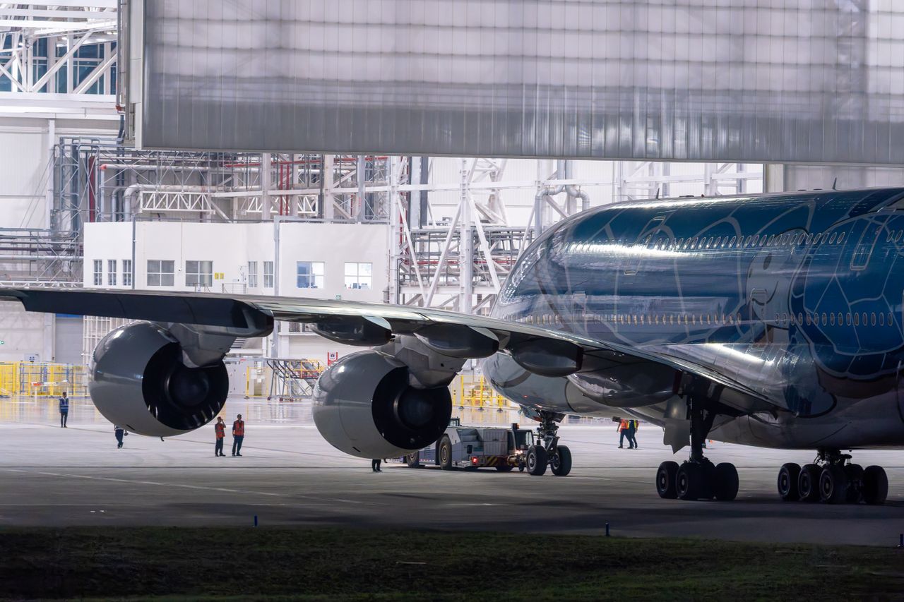 A large airplane inside a hangar with technicians and support vehicles nearby.